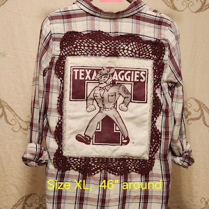 May include: A long-sleeve button-down shirt in a maroon and white plaid pattern. The back features a large white square patch with a graphic of the Texas Aggies mascot, framed by dark maroon crochet lace. The shirt is labeled size XL, 46 inches around.