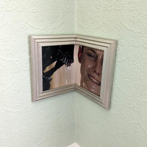 Puede incluir: Un marco de fotos plateado con una imagen dividida de una persona y una criatura. La persona sonríe y la criatura gotea un líquido.