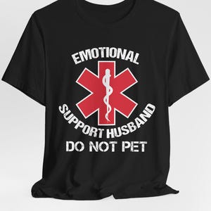 May include: Black t-shirt with a red medical symbol and the text "Emotional Support Husband Do Not Pet".