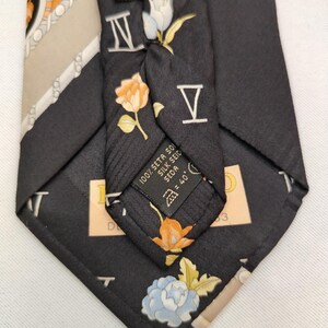 May include: Black silk tie with floral and Roman numeral designs. The tie features orange, white, and blue flowers, along with the Roman numerals IV and V. The label reads "100% Seta 501 Silk Seid = 40'".