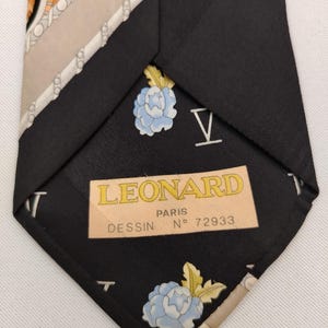 May include: Black silk tie with a floral and geometric pattern. The tie features a light blue flower design and the text "LEONARD PARIS". The tie is a classic accessory.