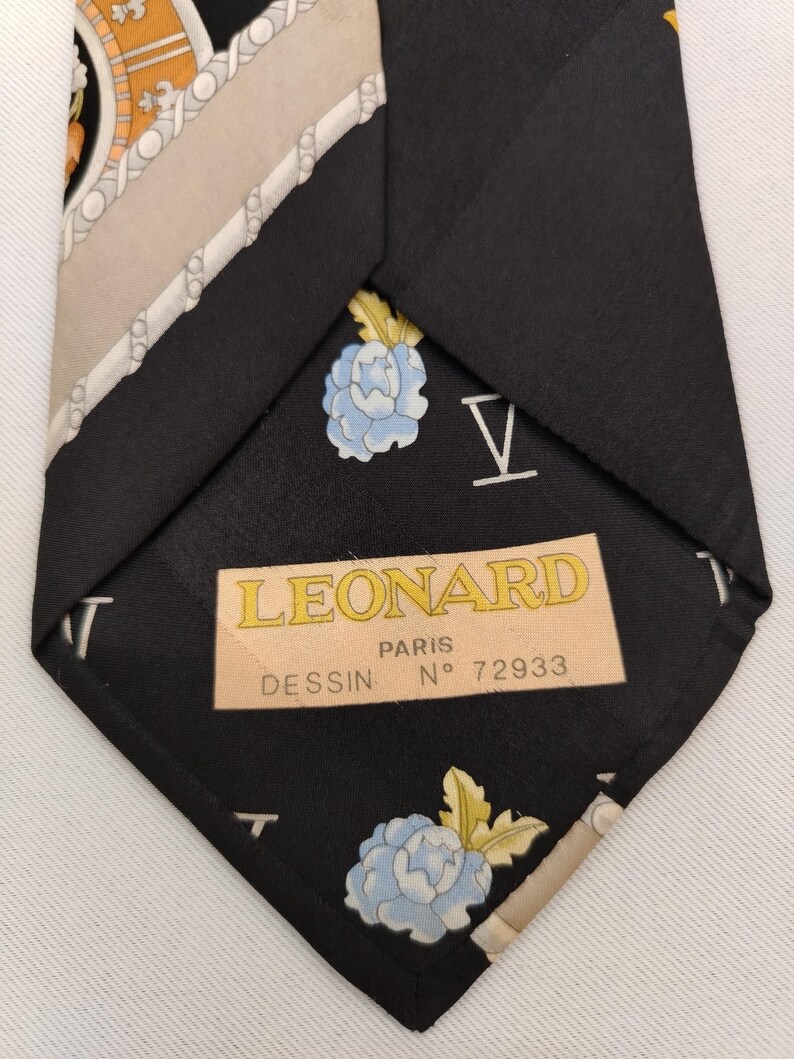 May include: Black silk tie with a floral and geometric pattern. The tie features a light blue flower design and the text "LEONARD PARIS". The tie is a classic accessory.