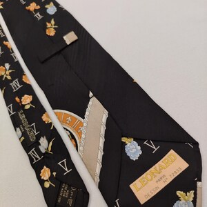 May include: Black silk tie with floral and Roman numeral patterns. The tie features a label that reads "LEONARD PARIS". The tie has a repeating pattern of orange and blue flowers.