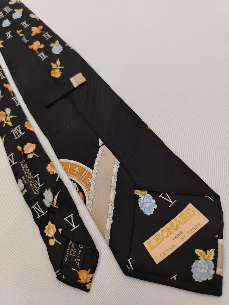 May include: Black silk tie with floral and Roman numeral patterns. The tie features a label that reads "LEONARD PARIS". The tie has a repeating pattern of orange and blue flowers.