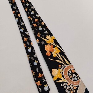 May include: Black necktie with a floral and clock face design. The tie features orange, yellow, and blue flowers, Roman numerals, and a beige stripe. The tie is a classic accessory.