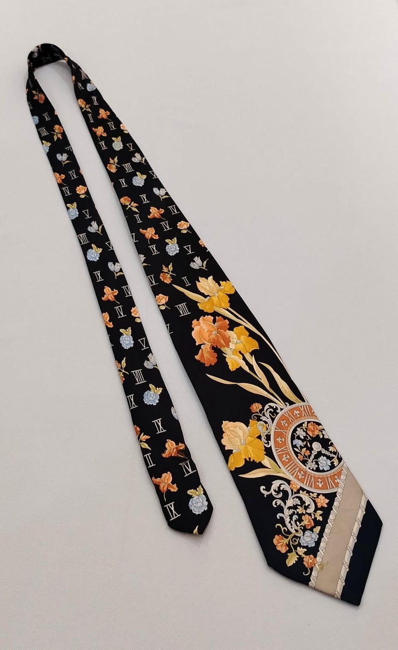 May include: Black necktie with a floral and clock face design. The tie features orange, yellow, and blue flowers, Roman numerals, and a beige stripe. The tie is a classic accessory.
