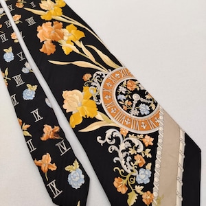 May include: Black silk tie with a floral and clock face design. The tie features orange, yellow, and blue flowers, Roman numerals, and a beige stripe. The tie is a classic accessory.