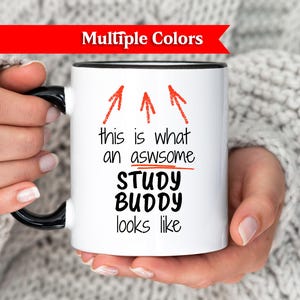 Puede incluir: Una taza de cerámica blanca con un asa negra y el texto "But First, Coffee" en negrita negra. La taza se encuentra sobre un fondo neutro, resaltando su diseño sencillo.