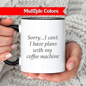 Può includere: Tazza da caffè bianca con manico e bordo neri, tenuta da una persona. La tazza ha il testo "Sorry...I can't. I have plans with my coffee machine." Uno striscione rosso in alto dice "Multiple Colors".