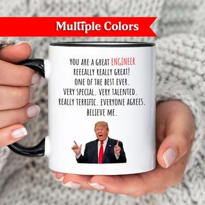Peut inclure: Mug en céramique blanche avec une anse et un bord noirs, avec le texte "YOU ARE A GREAT ENGINEER" et une caricature d'un homme en costume. La tasse a une bannière rouge qui dit "Multiple Colors".