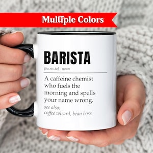 Op de afbeelding: Witte koffiemok met een zwarte handgreep en rand, met het woord "BARISTA" in zwarte letters. De mok bevat een definitie en gerelateerde termen. Een rode banner bovenaan leest "Multiple Colors".