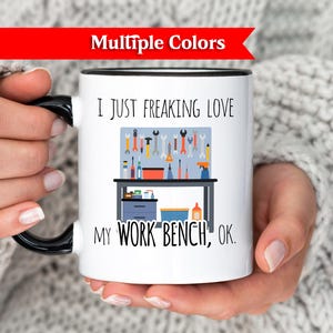 May include: White ceramic mug with a black handle and rim, featuring the text "I JUST FREAKING LOVE MY WORK BENCH, OK." The mug has a graphic of a workbench with tools. A red banner at the top says "Multiple Colors."