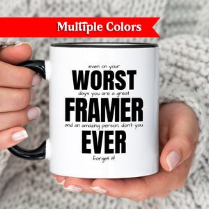 Könnte beinhalten: Weiße Keramik-Tasse mit schwarzem Griff und Rand, mit dem Text "WORST FRAMER EVER" in schwarzer Schrift. Die Tasse hat die Worte "Multiple Colors" auf einem roten Banner.