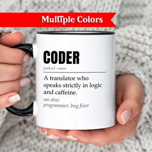 May include: White coffee mug with black handle and rim, featuring the word "CODER" and a definition. The text includes "A translator who speaks strictly in logic and caffeine." The mug is held by a person.