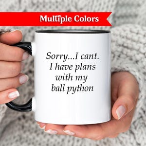 Könnte beinhalten: Weiße Keramik-Tasse mit schwarzem Henkel und Rand, mit dem Text "Sorry...I cant. I have plans with my ball python." Ein rotes Banner oben zeigt "Multiple Colors."