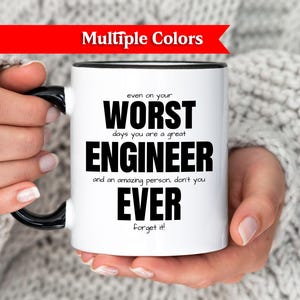 Könnte beinhalten: Weißer Keramikbecher mit schwarzem Henkel und Rand, mit dem Text "WORST ENGINEER EVER" in Schwarz. Der Becher wird von einer Person gehalten, die einen weißen Pullover trägt. Ein rotes Banner oben zeigt "Multiple Colors".