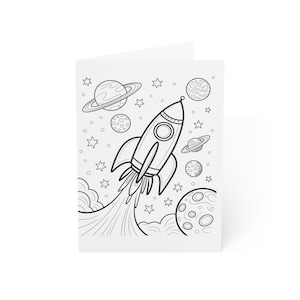 May include: A black and white line drawing of a rocket ship blasting off into space, surrounded by planets, stars, and clouds. The rocket has a circular window and a pointed top. The card is white and folded.