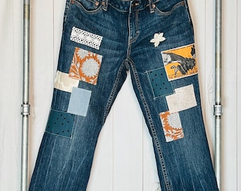 May include: Blue denim jeans with various fabric patches sewn on. The patches include floral patterns, geometric designs, and a small piece of text that reads "The Mystery of Dark Ho."