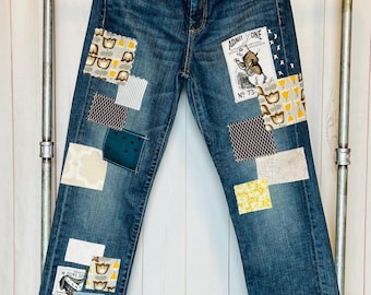 May include: Blue denim jeans with various fabric patches sewn on. The patches include a white rabbit illustration with the text "ADMIT ONE NO. 73", a floral pattern, and a geometric pattern.