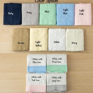 May include: A variety of folded blankets in various colors, including navy, grey, mint, light blue, and light pink. Additional colors are brown, light yellow, white, and ivory. The image also shows white blankets with colored trim in blue, mint, pink, and grey.