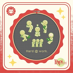 Könnte beinhalten: Kreuzstichmuster mit einer Gruppe von pixelartigen Figuren, die zusammenarbeiten. Das Muster ist in einem roten Rahmen eingefasst und enthält den Text "Hard @ work."