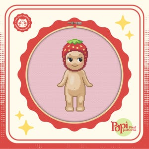 May include: A cross-stitch pattern featuring a cartoon baby wearing a red strawberry hat. The pattern is framed in a red hoop with a white background. The image is surrounded by a white border with a red polka dot pattern.