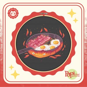 Könnte beinhalten: Ein Kreuzstichmuster einer Bratpfanne mit Speck und Eiern, die in Flammen stehen. Die Pfanne hat ein lächelndes Gesicht. Das Muster ist in einem roten Reifen mit weißem Hintergrund gerahmt. Das Bild enthält den Text "Pop! Pixel patterns".