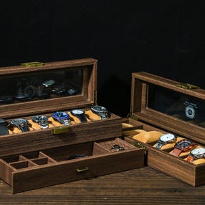 May include: A wooden watch box with a glass top and a drawer. The box has a brown finish and is filled with watches. The box is on a wooden surface.