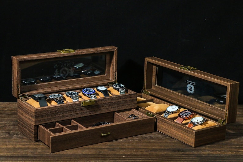 May include: A wooden watch box with a glass top and a drawer. The box has a brown finish and is filled with watches. The box is on a wooden surface.
