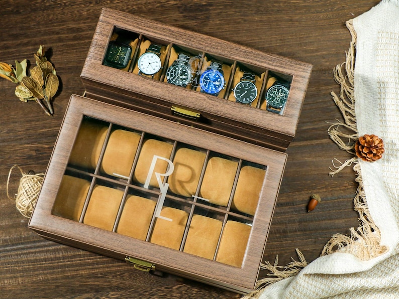 May include: A wooden watch box with a glass top and a bottom drawer. The top drawer has 6 slots for watches and the bottom drawer has 10 slots. The box is engraved with the initials "R.L."