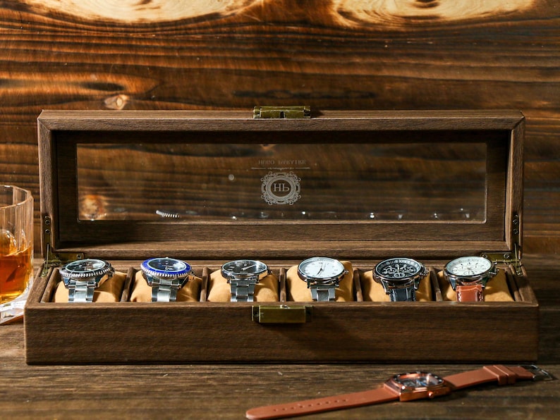 May include: A wooden watch box with a glass top and eight slots for watches. The box is closed and the watches are visible through the glass. The box is made of dark wood and has a brass latch.