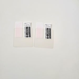 May include: Two clear screen protectors with attached labels. Each label reads "FRONT 2" and includes instructions to peel off the mask. The protectors are rectangular with rounded corners, designed for a device screen.