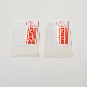 May include: Two screen protector films with attached stickers. The stickers are red and white, with the word "BACK" and the number "1" printed on them. The text on the sticker reads "THIS STICKER HELPS TO REMOVE THE MASK FROM THE SCREEN GUARD".