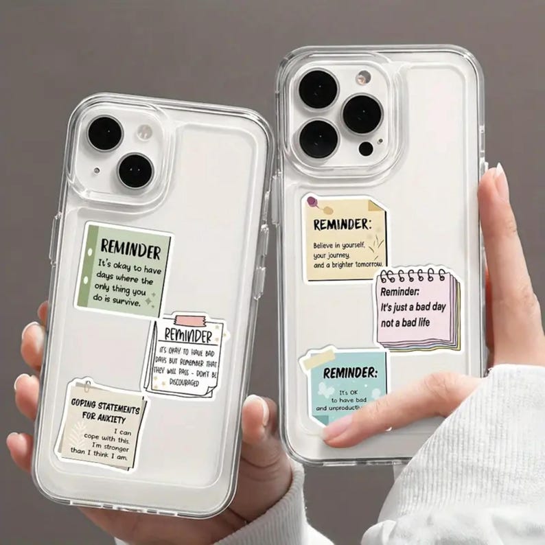 May include: Two clear phone cases with colourful motivational reminder stickers. The stickers have text such as "It's okay to have days where the only thing you do is survive." and "Believe in yourself, your journey, and a brighter tomorrow."