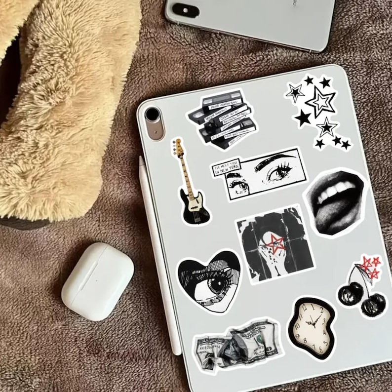 May include: A white tablet with various black and white stickers. The stickers include a bass guitar, a heart with an eye, a clock, a mouth, and a hand with a star. The text on one sticker reads "I'll meet you in New York".