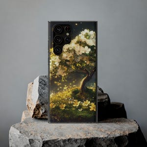 May include: A black phone case with a floral design. The case features a white tree with yellow flowers and glowing lights in the background.