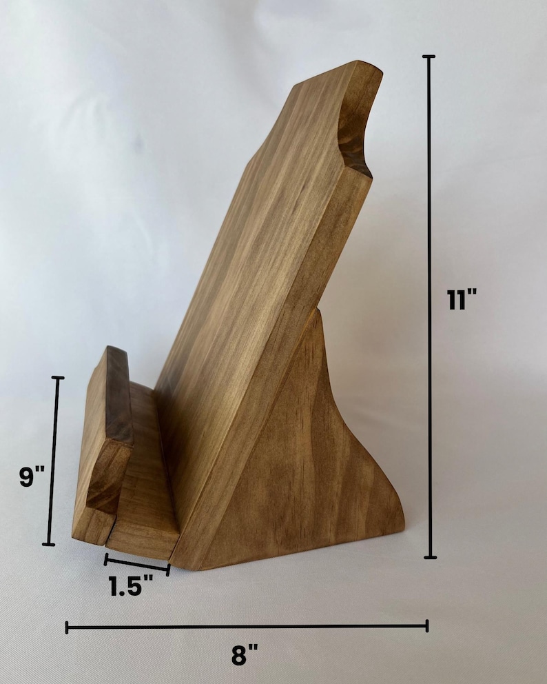 May include: A wooden book stand with a natural finish. It measures 11 inches tall, 9 inches wide, and 8 inches long. The stand has a 1.5 inch wide base.