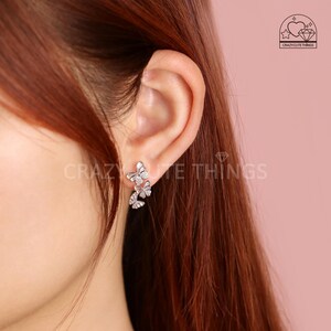 May include: Silver butterfly earrings with clear cubic zirconia stones. The earrings are dangling and feature three butterflies.