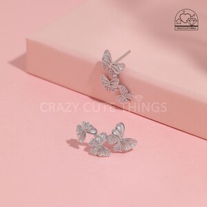 May include: A pair of silver butterfly earrings with clear crystal accents. The earrings are designed with three butterflies stacked on top of each other.