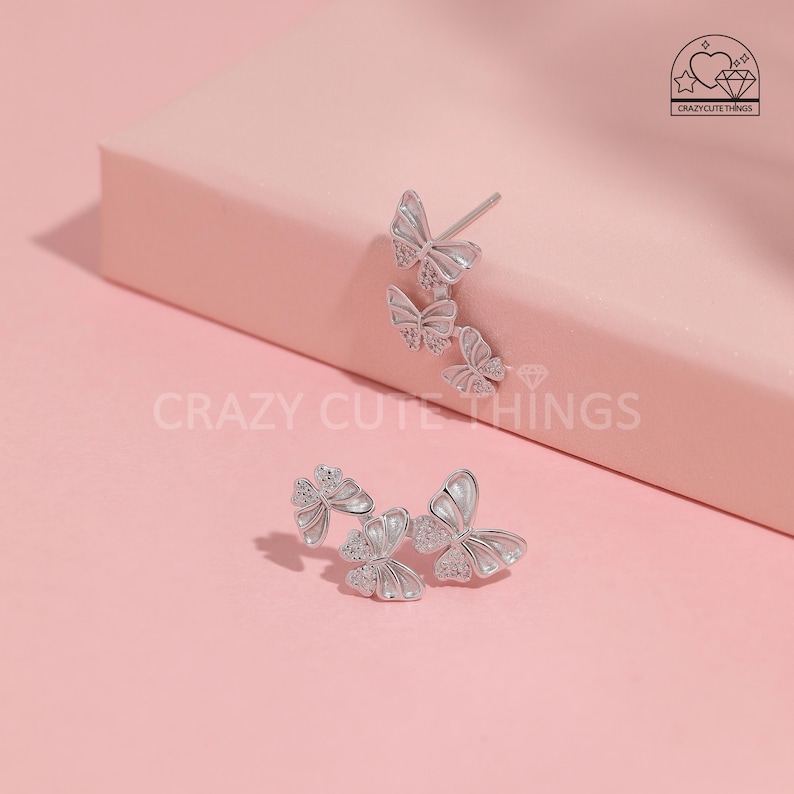 May include: A pair of silver butterfly earrings with clear crystal accents. The earrings are designed with three butterflies stacked on top of each other.