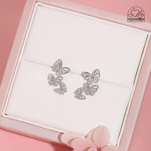 May include: Silver butterfly earrings with cubic zirconia stones. The earrings feature three butterflies stacked on top of each other.