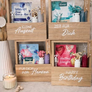 Könnte beinhalten: Vier Geschenkboxen aus Holz mit verschiedenen Artikeln, darunter Badeprodukte, kleine Vasen und dekorative Elemente. Jede Box trägt eine andere Botschaft in weißer Schrift: "KLEINE Auszeit", "ZEIT FÜR Dich", "FÜR DICH von Herzen" und "HAPPY Birthday".
