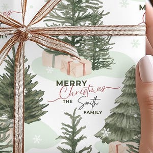 May include: Christmas gift wrap featuring a watercolor-style design of green pine trees, snowflakes, and small gift boxes on a light green and white background. The text 'Merry Christmas The Smith Family' is printed on the wrap in elegant cursive and simple block lettering. The design is festive and suitable for the holiday season.