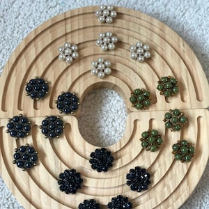 May include: Assortment of black, green and white flower-shaped earrings with pearl and rhinestone embellishments displayed on a wooden circular stand.
