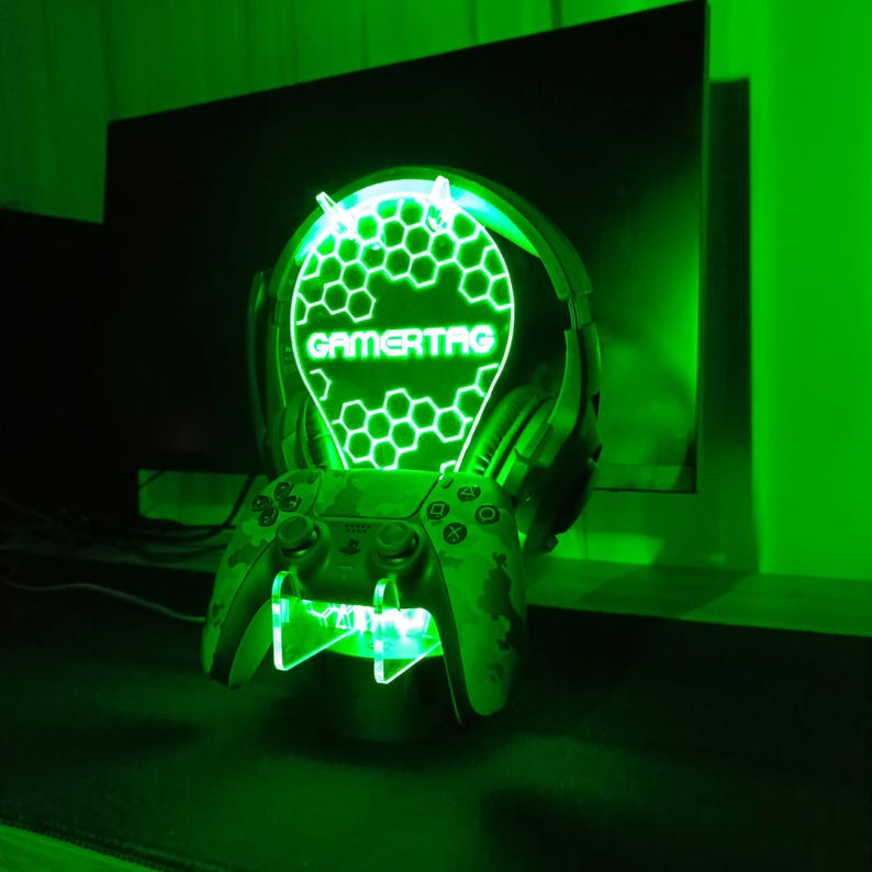 May include: A green gamertag light with a honeycomb design and the word "GAMERTAG" in the center. The light is mounted on a stand with a camouflage-patterned video game controller.