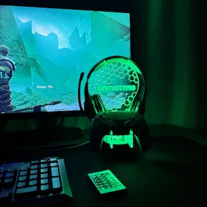 May include: A green gamer themed light with a headset and controller stand. The light has a honeycomb pattern and the word "GAMERTAG" is visible. The light is on a desk with a keyboard and a remote control.