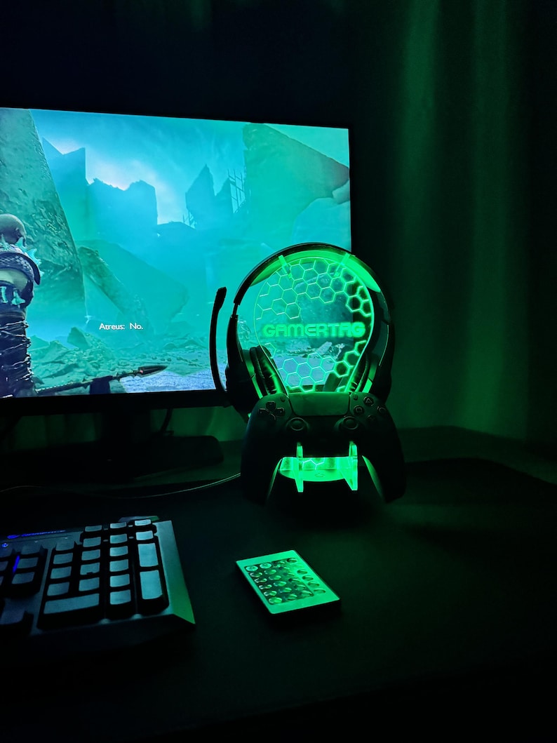 May include: A green gamer themed light with a headset and controller stand. The light has a honeycomb pattern and the word "GAMERTAG" is visible. The light is on a desk with a keyboard and a remote control.
