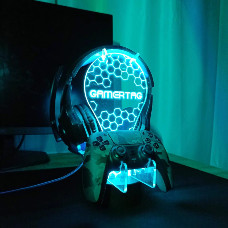 May include: A blue and black gaming headset stand with a gamertag inscription and a camouflage-patterned video game controller.