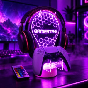 Può includere: Un paio di cuffie da gaming nere poggiano su un supporto LED circolare con un motivo a nido d'ape viola luminoso e la scritta GAMERTAG. Un controller di gioco bianco è posizionato sulla base, insieme a un piccolo telecomando con tasti colorati.
