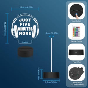 May include: A white acrylic night light with the text "Just Five Minutes More" and a headphone graphic. The light has a black base and comes with a remote control and a USB charging cable. It can also be powered by three AAA batteries.